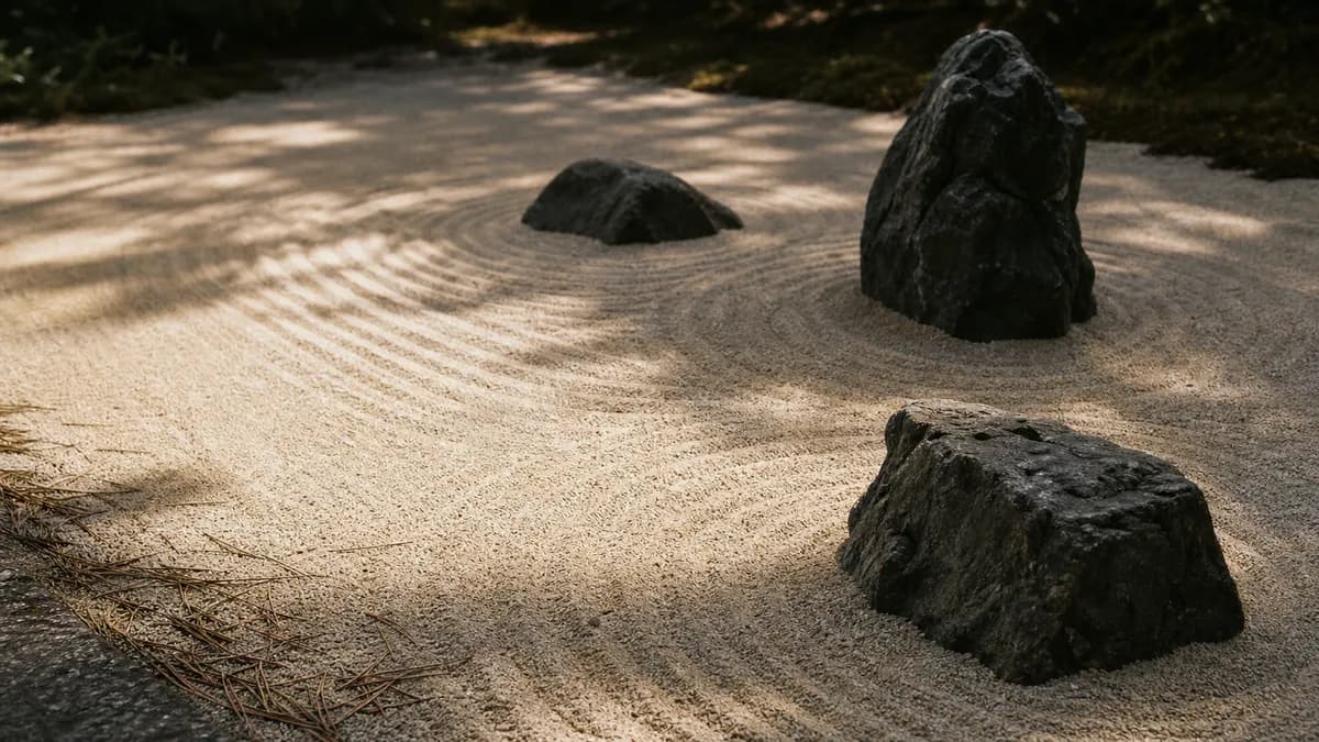 Three dark stones rest in raked concentric gravel patterns in a quiet zen garden, soft pine shadows across the sand.